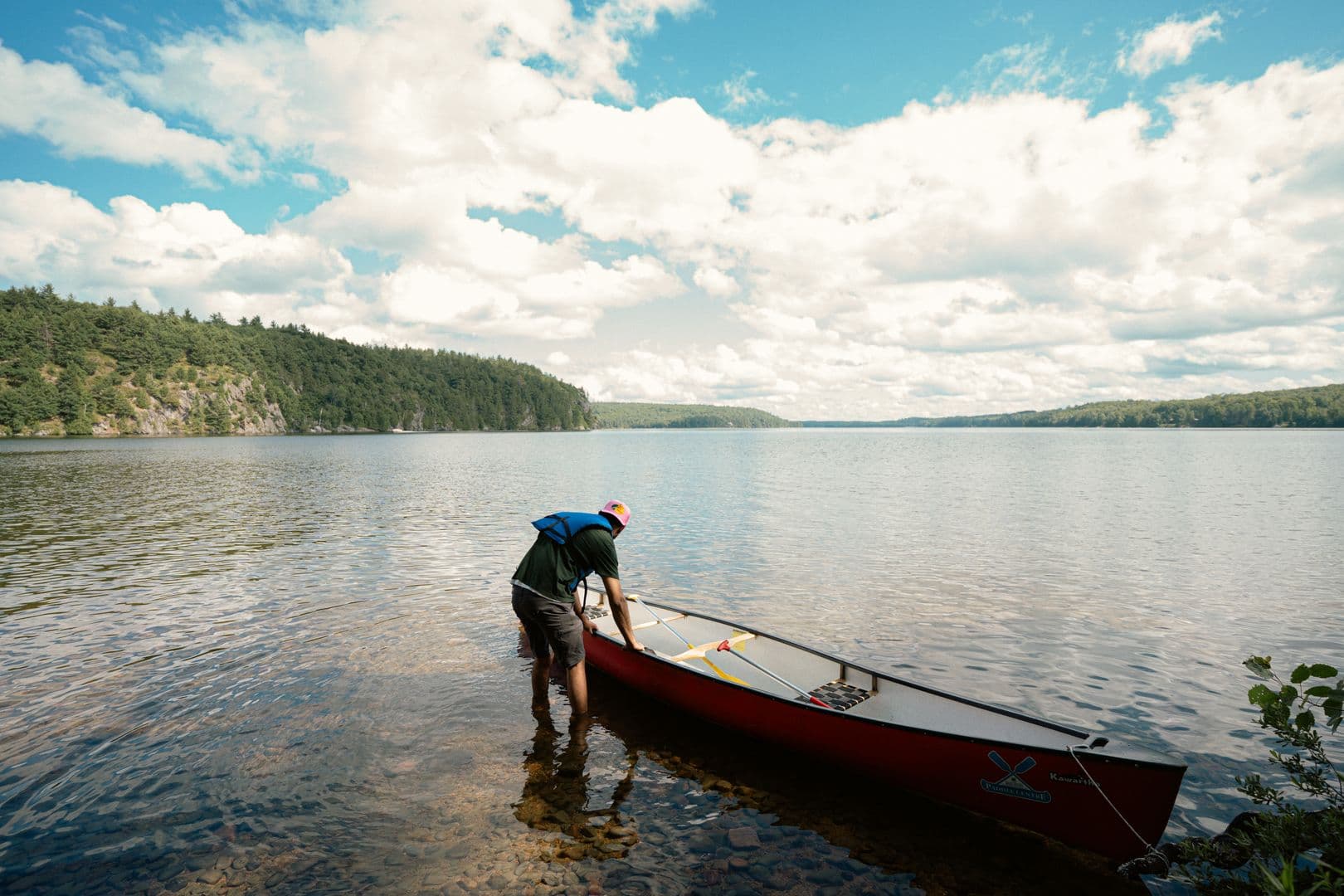 A paddler launching a red canoe from a rocky Ontario shoreline